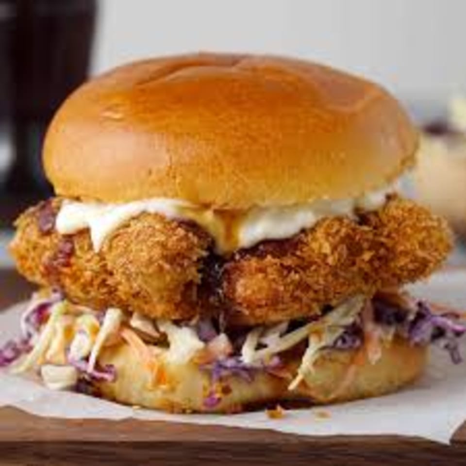 Crispy fried chicken sandwich with coleslaw and white sauce on a brioche bun.